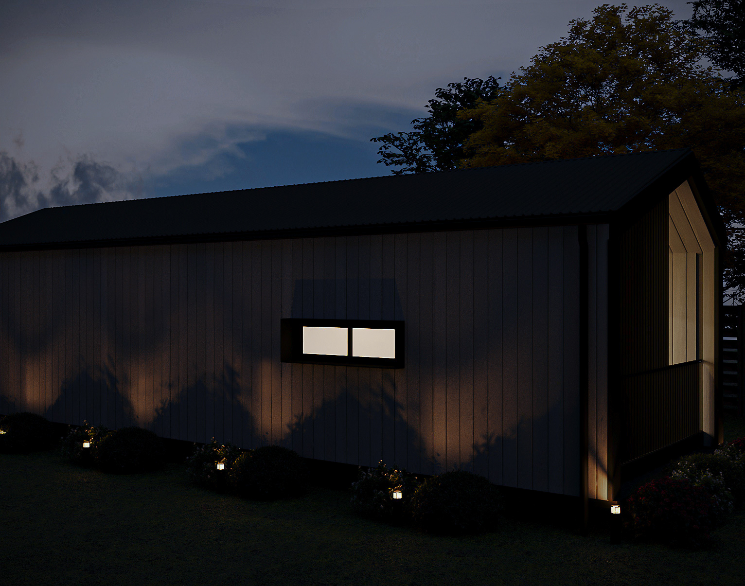 Evening porch view with warm wall sconce lighting illuminating the entrance door and timber deck (Lexicon Half light grey vertical cladding with dark Basalt roof and trim, captured at twilight under warm architectural lighting).